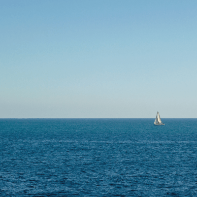 A sailboat on the horizon under a clear blue sky and calm sea.