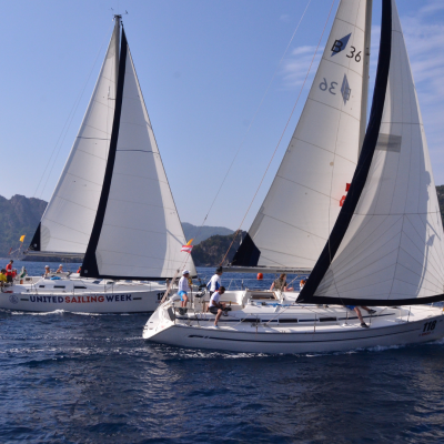 Two sailboats racing in open water with mountains in the background.