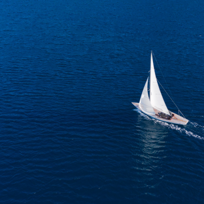 Aerial view of a sailboat on a vast, calm blue sea.